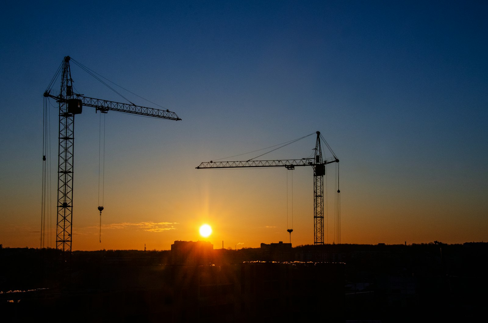 A tower crane in silhouette against first light — the site Construction Pulse keeps on budget